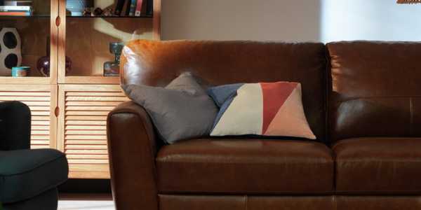 A brown leather sofa with mismatching cushions.